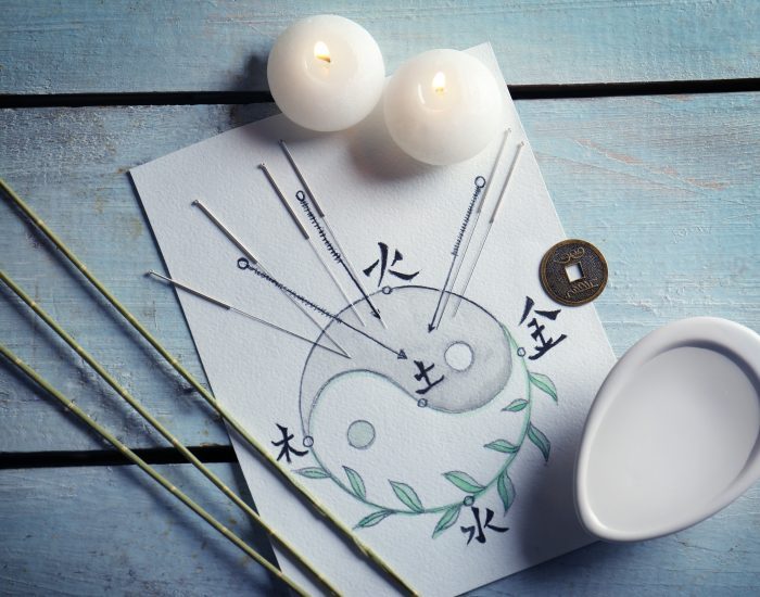 Acupuncture needles with candles and drawing on wooden background